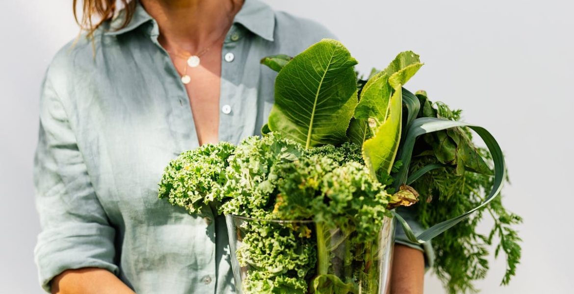 A woman in a light shirt carrying a basket of fresh greens, symbolizing healthy eating and lifestyle.