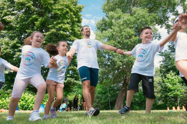 Group of joyful children playing outdoors with an instructor in a sunny park.